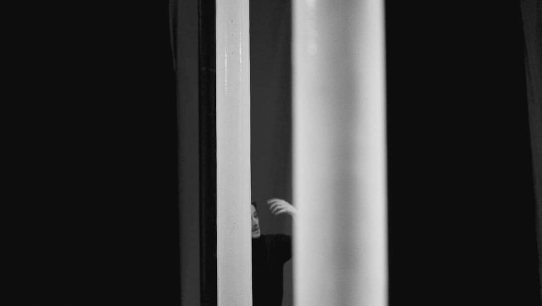 Image of an actor visible between curtains in black and white